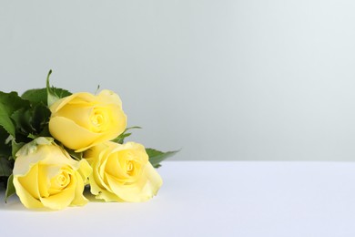 Photo of Beautiful fresh yellow roses on white table against light grey background. Space for text