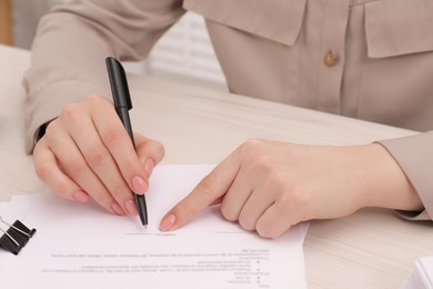 Photo of Woman signing document at wooden table, closeup