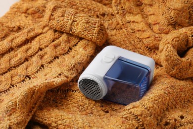 Photo of Modern fabric shaver on orange knitted sweater, closeup