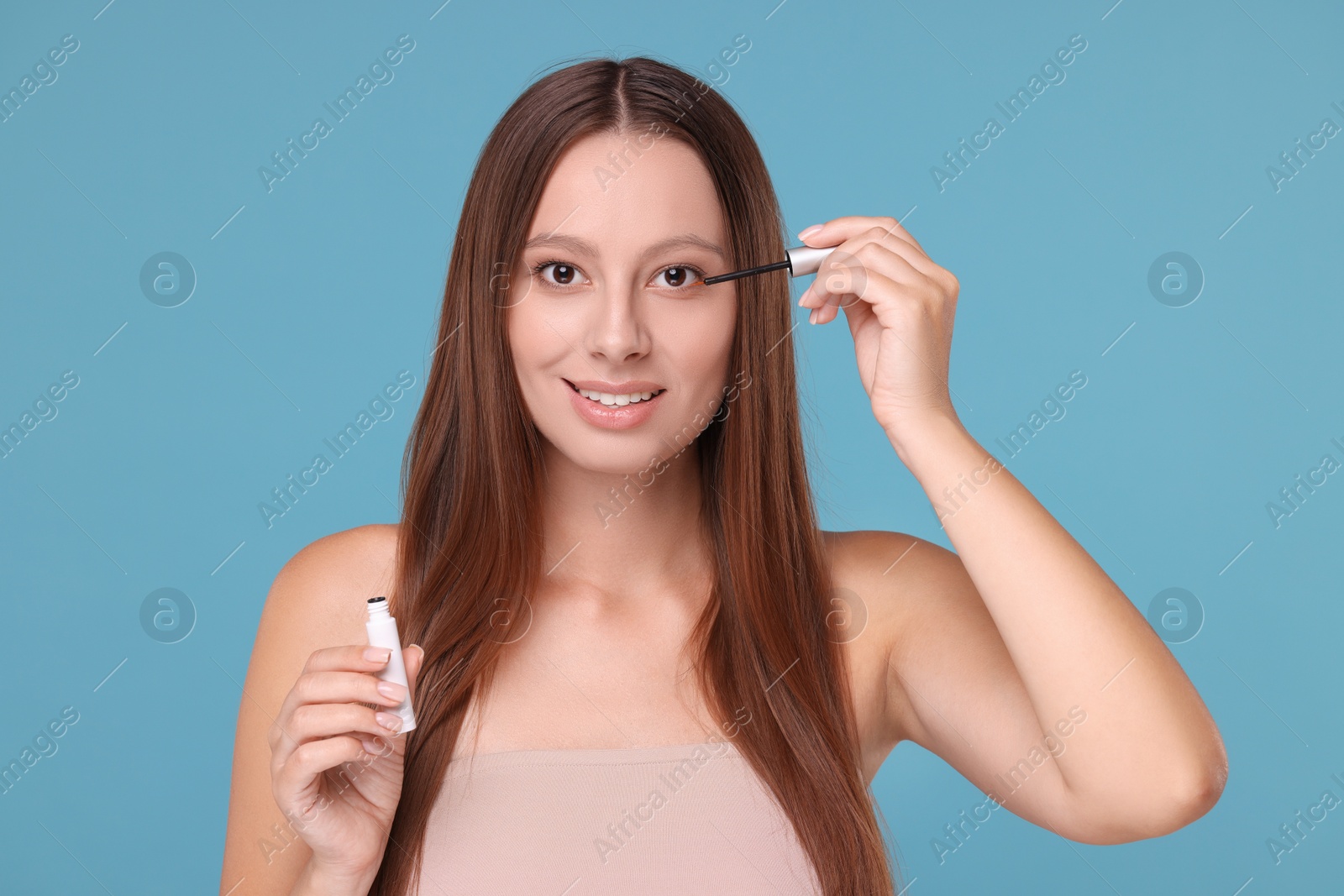 Photo of Beautiful woman applying serum onto eyelashes on light blue background