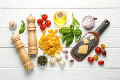 Photo of Pile of pasta, grater, shakers and products on white wooden table, flat lay