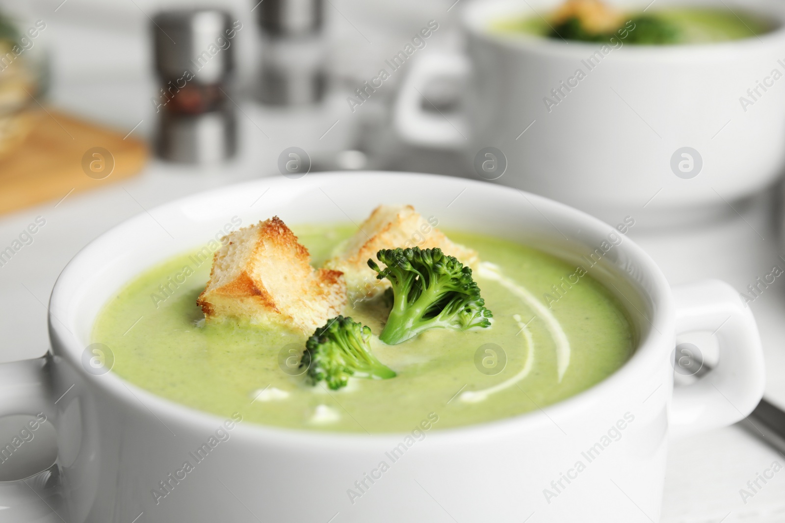 Photo of Bowl of delicious broccoli cream soup with croutons on table, closeup