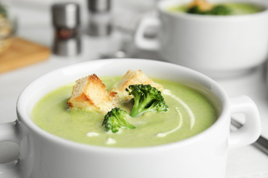 Photo of Bowl of delicious broccoli cream soup with croutons on table, closeup
