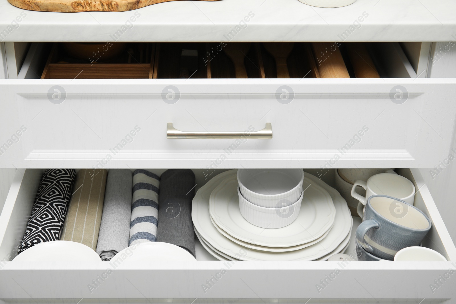 Photo of Open drawers of kitchen cabinet with different dishware and towels