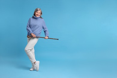 Photo of Senior woman with walking cane on light blue background, space for text