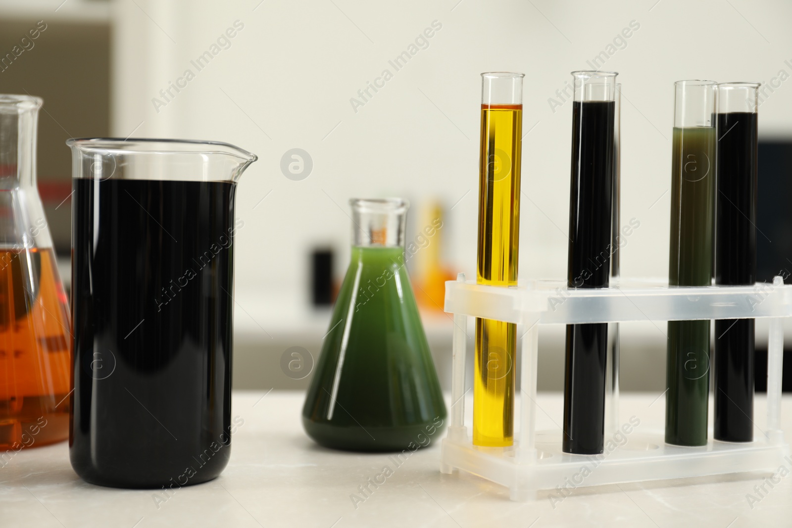 Photo of Laboratory glassware with different types of crude oil on light marble table