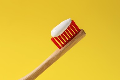 Wooden brush with toothpaste on yellow background, closeup