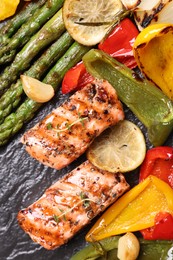 Tasty grilled salmon with lemon and vegetables on black slate, top view