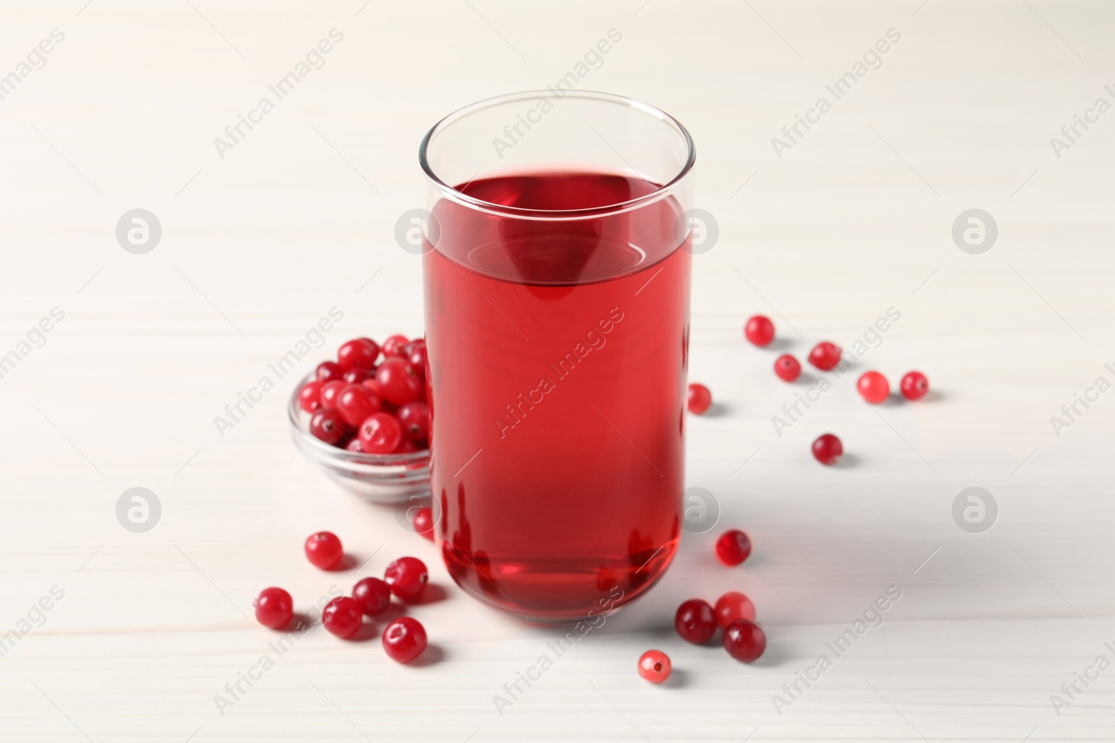 Photo of Tasty cranberry juice in glass and fresh berries on white wooden table