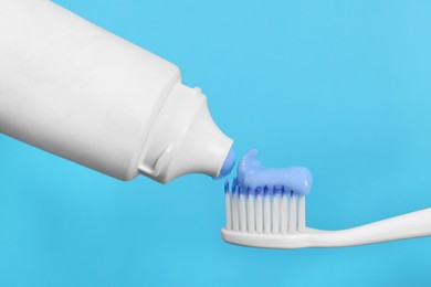 Applying paste on toothbrush against light blue background, closeup