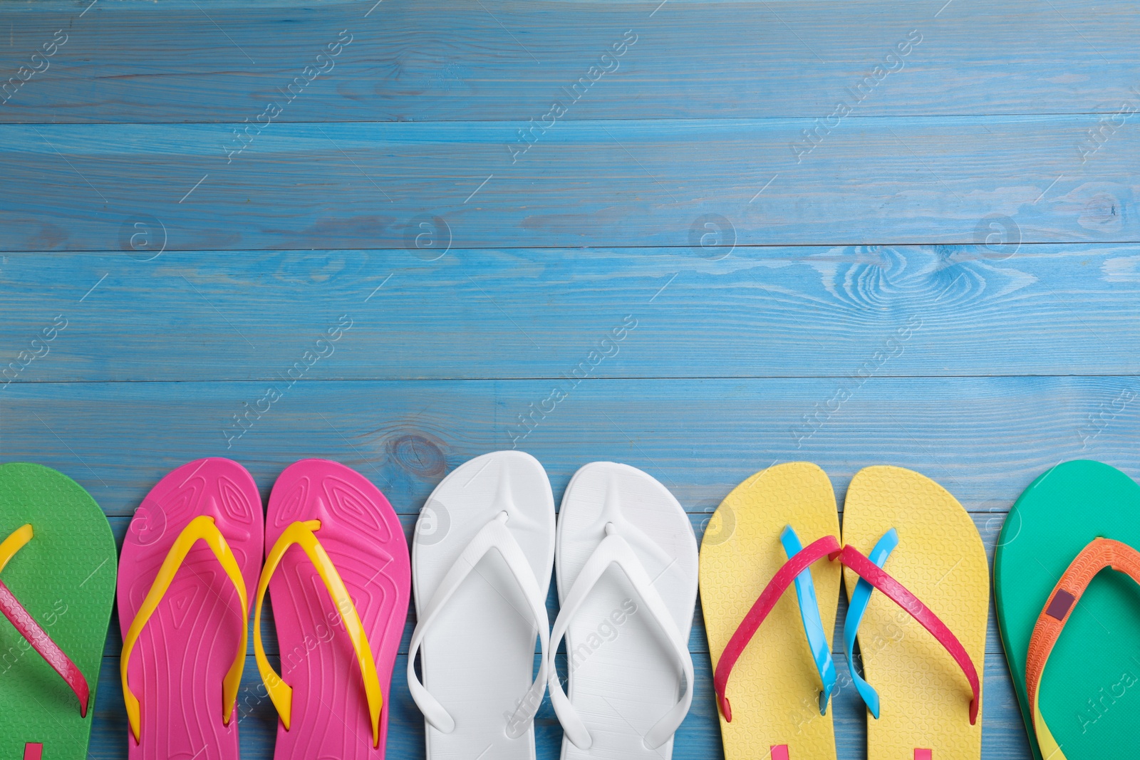 Photo of Many different flip flops on light blue wooden background, flat lay. Space for text