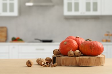 Fresh pumpkins and walnuts on wooden table in kitchen, space for text