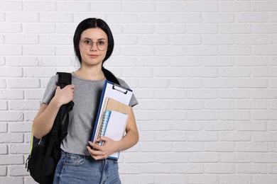 Student with notebooks, clipboard and backpack near white brick wall. Space for text