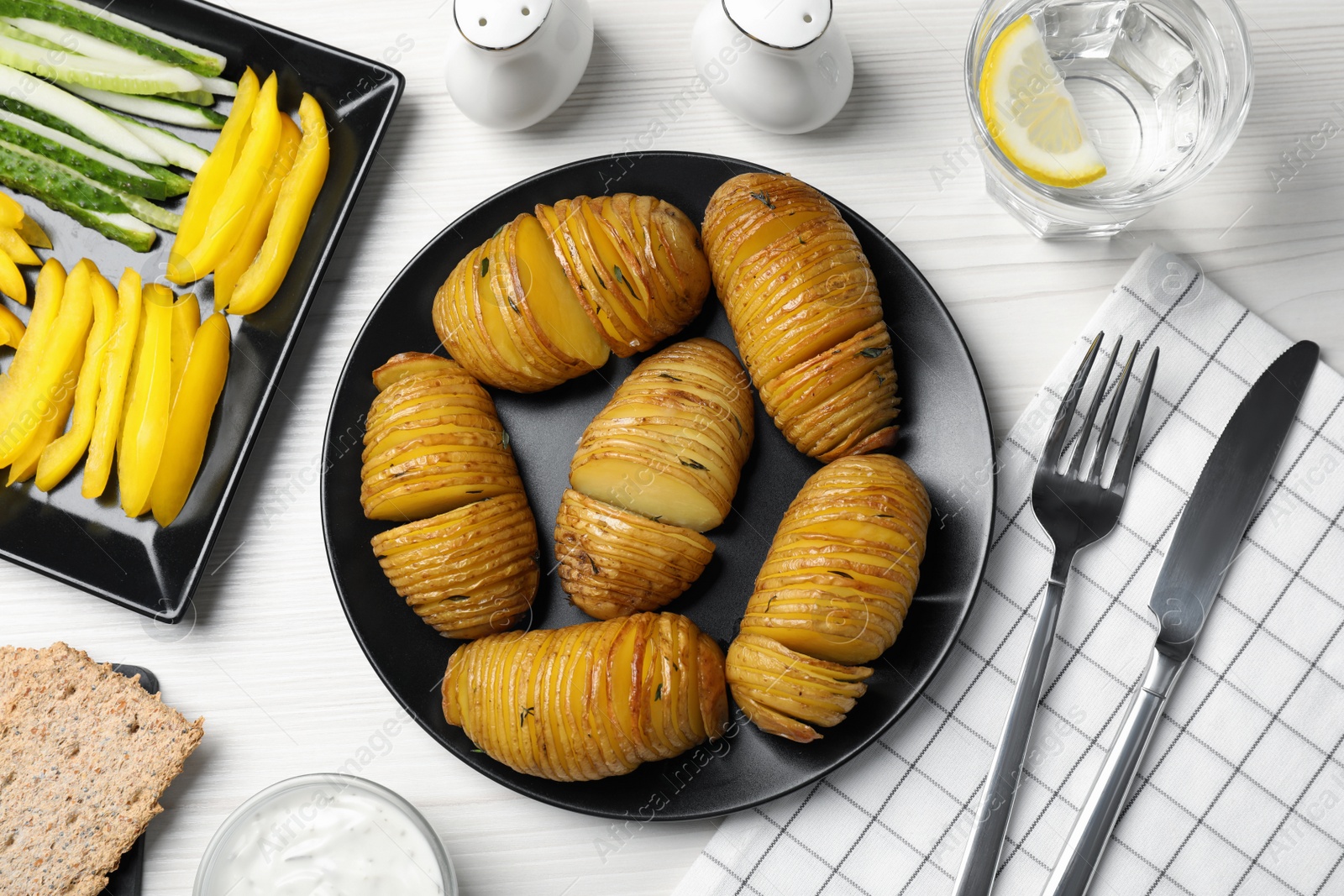 Photo of Delicious homemade Hasselback potatoes served on white wooden table, flat lay