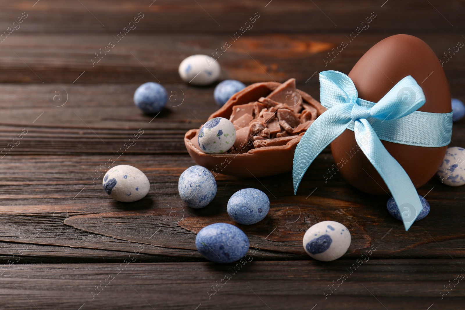 Photo of Tasty chocolate egg with light blue bow and sweets on wooden table