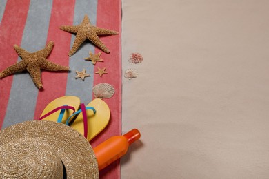 Photo of Beach towel, hat, sunscreen, starfishes, sea shells and flip flops on sand. Space for text