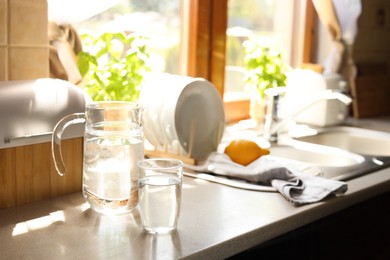 Photo of Jug and glass with water on countertop in kitchen, space for text