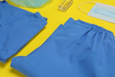 Photo of Medical uniform, face mask and antiseptic on yellow background, closeup view