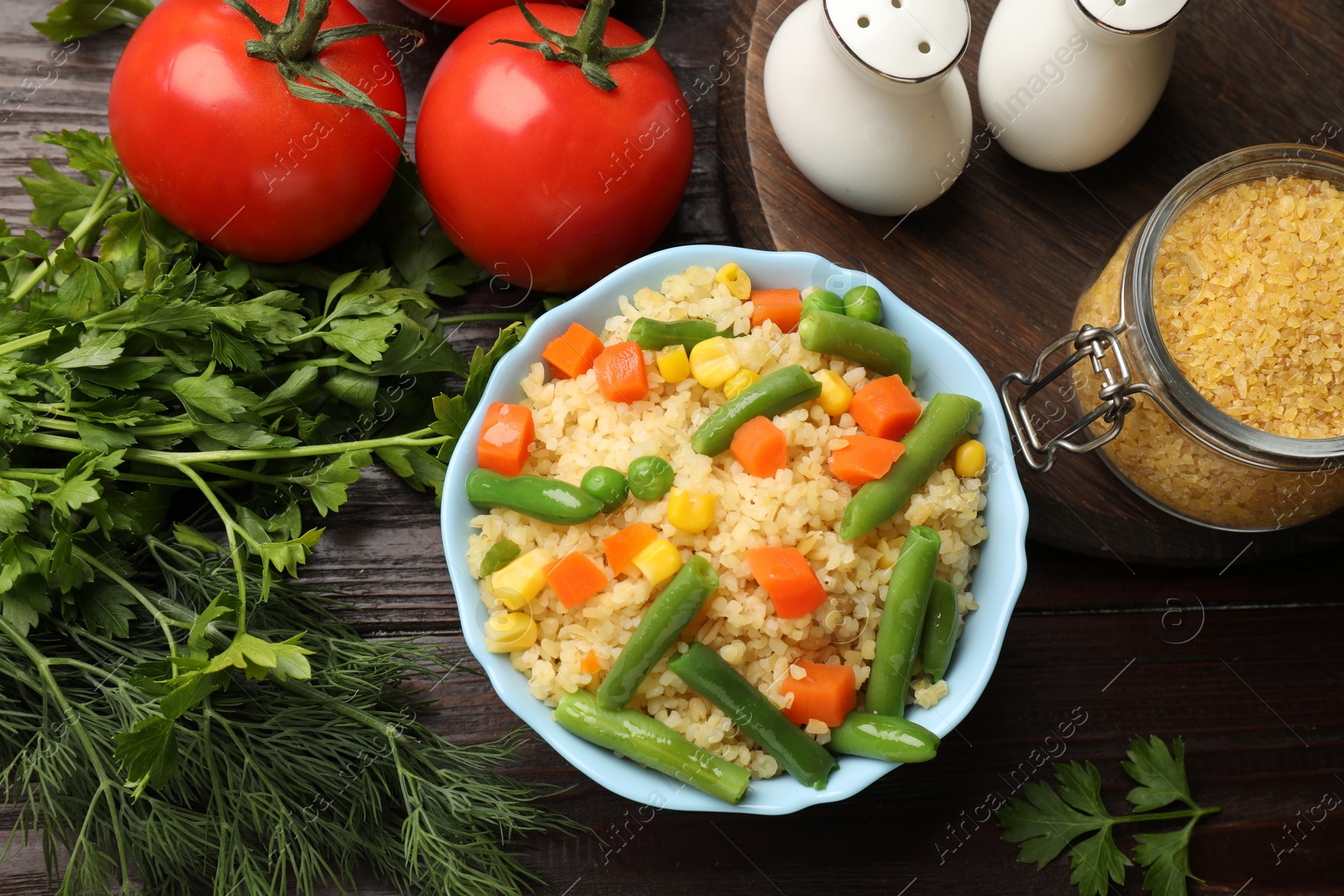 Photo of Delicious bulgur with vegetables in bowl and spices on table, flat lay