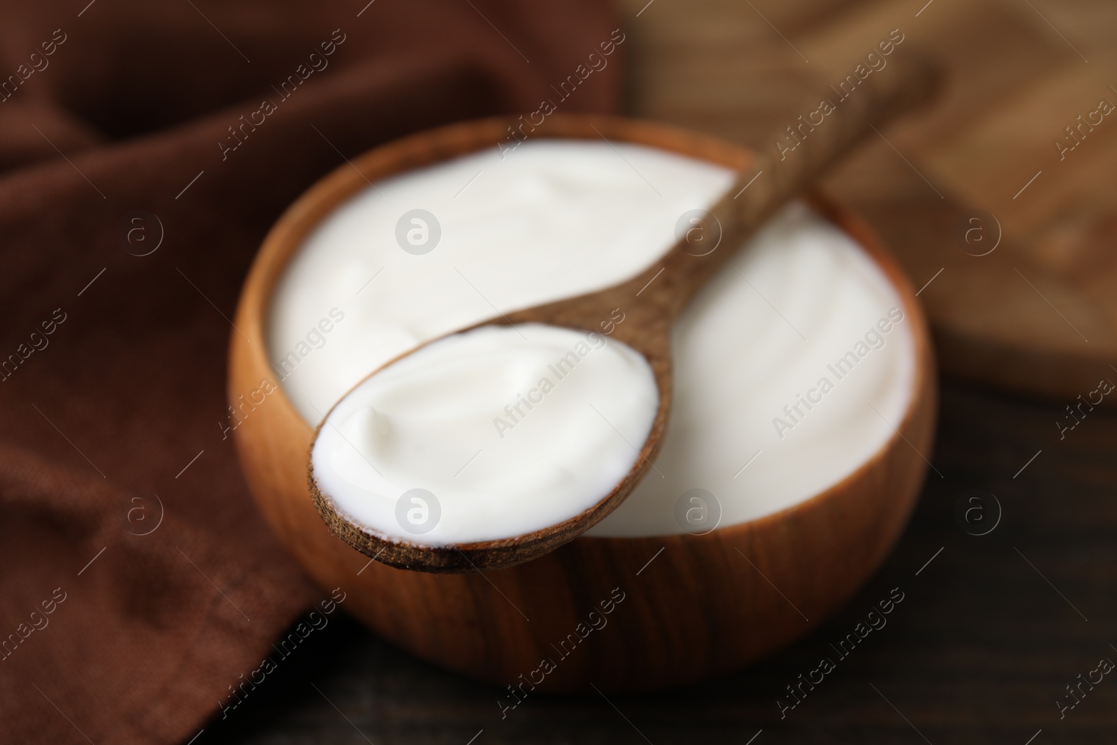 Photo of Delicious natural yogurt in bowl and spoon on wooden table, closeup