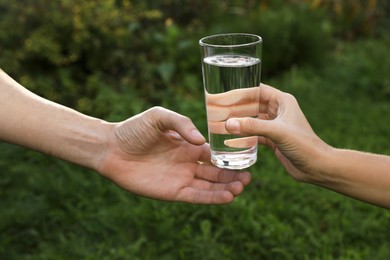 Photo of Woman giving glass of fresh water to man outdoors, closeup