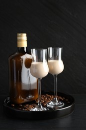 Coffee cream liqueur in glasses, bottle and beans on black wooden table