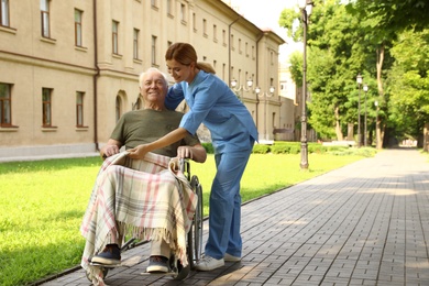 Photo of Happy nurse assisting elderly man in wheelchair at park