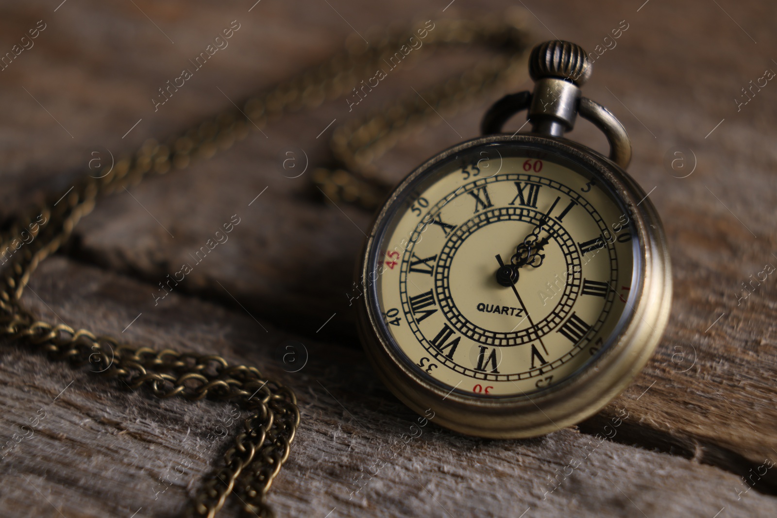 Photo of Pocket clock with chain on wooden table, closeup