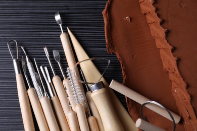 Clay and set of modeling tools on dark gray wooden table, flat lay