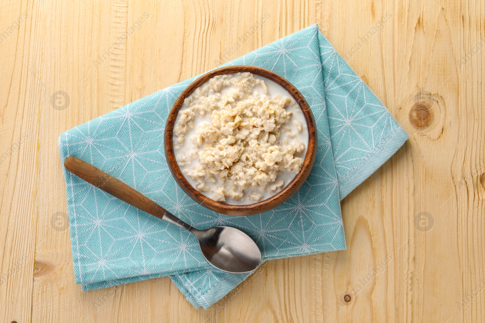 Photo of Tasty boiled oatmeal in bowl and spoon on wooden table, top view