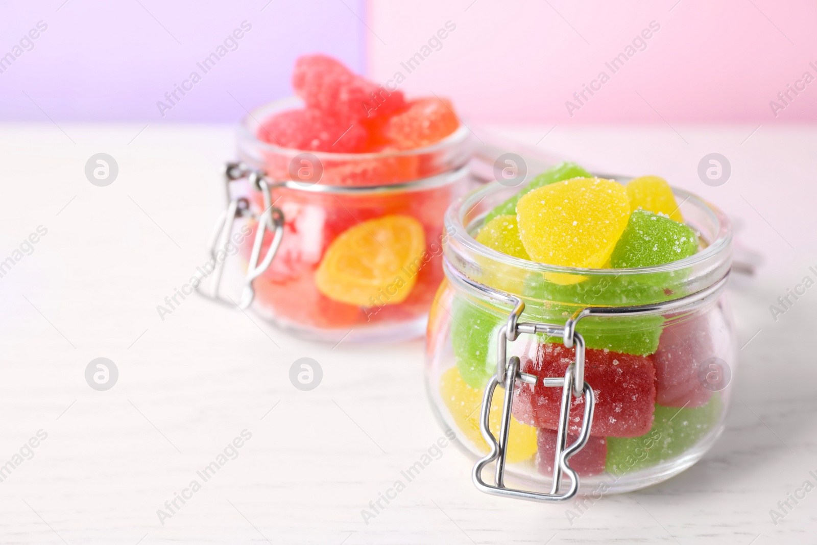 Photo of Yummy candies in glass jars on white table, space for text