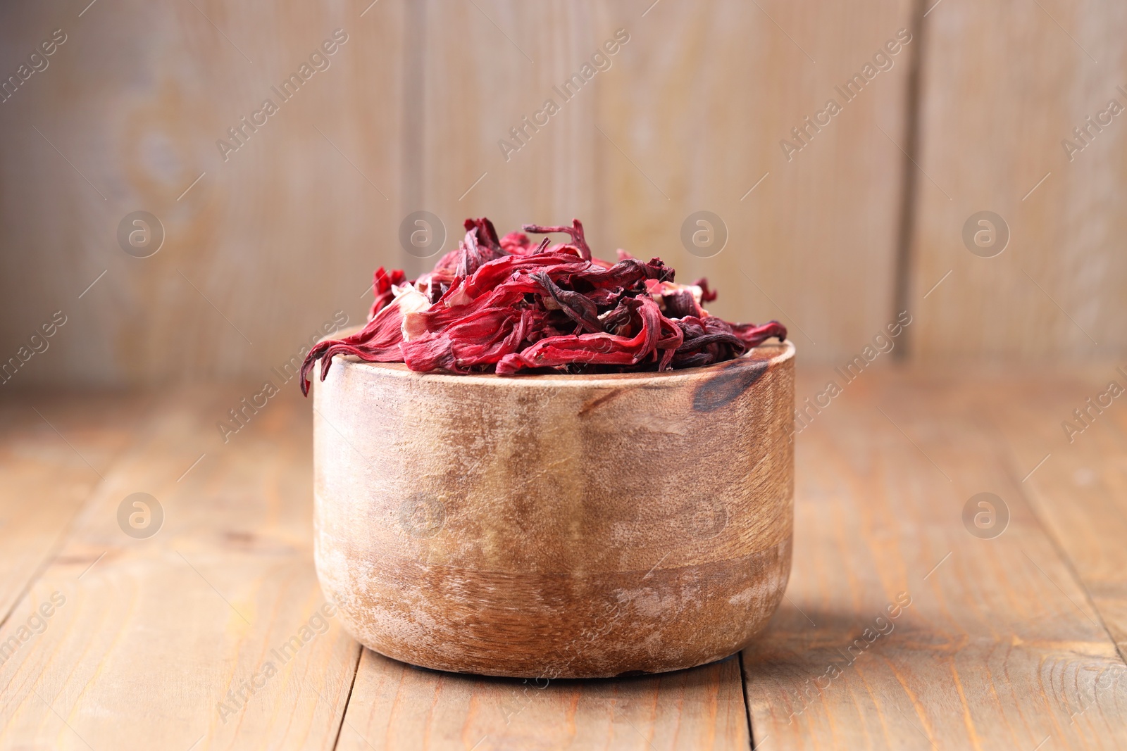 Photo of Dry hibiscus tea in bowl on wooden table