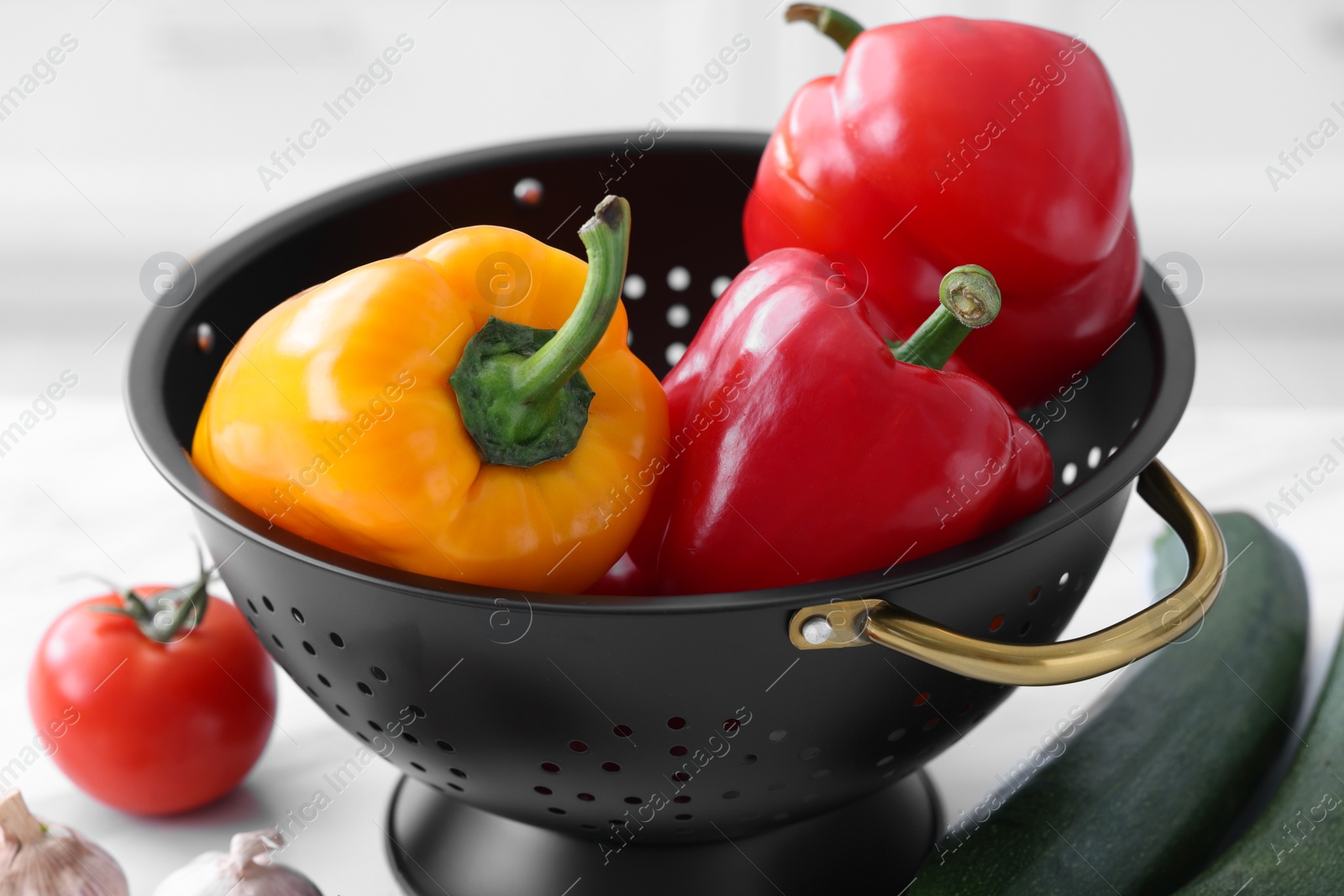 Photo of Black colander and different vegetables on white table, closeup