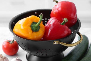 Black colander and different vegetables on white table, closeup