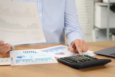 Photo of Accountant using calculator at wooden desk in office, closeup