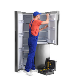 Male technician repairing refrigerator on white background