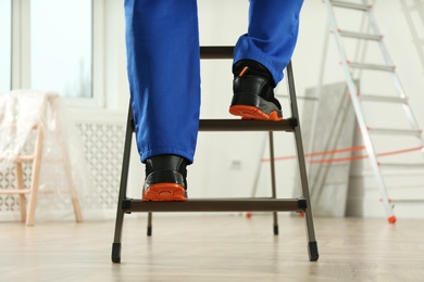 Professional worker climbing up ladder in room, closeup