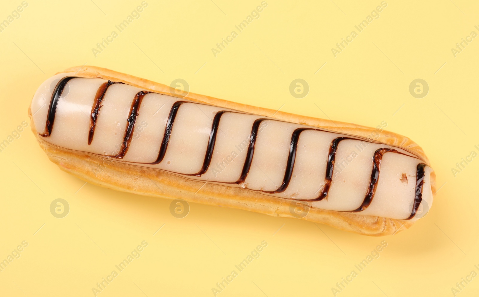 Photo of Delicious eclair covered with glaze on yellow background, top view