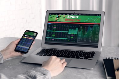 Image of Woman betting on sports using smartphone and laptop at table, closeup. Bookmaker websites on displays