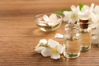 Photo of Jasmine essential oil and fresh flowers on wooden table, space for text