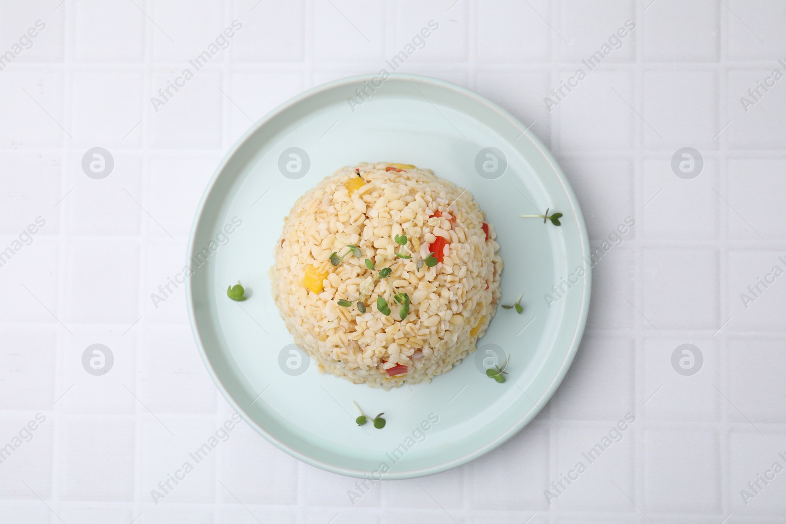 Photo of Delicious bulgur with vegetables and microgreens on white tiled table, top view