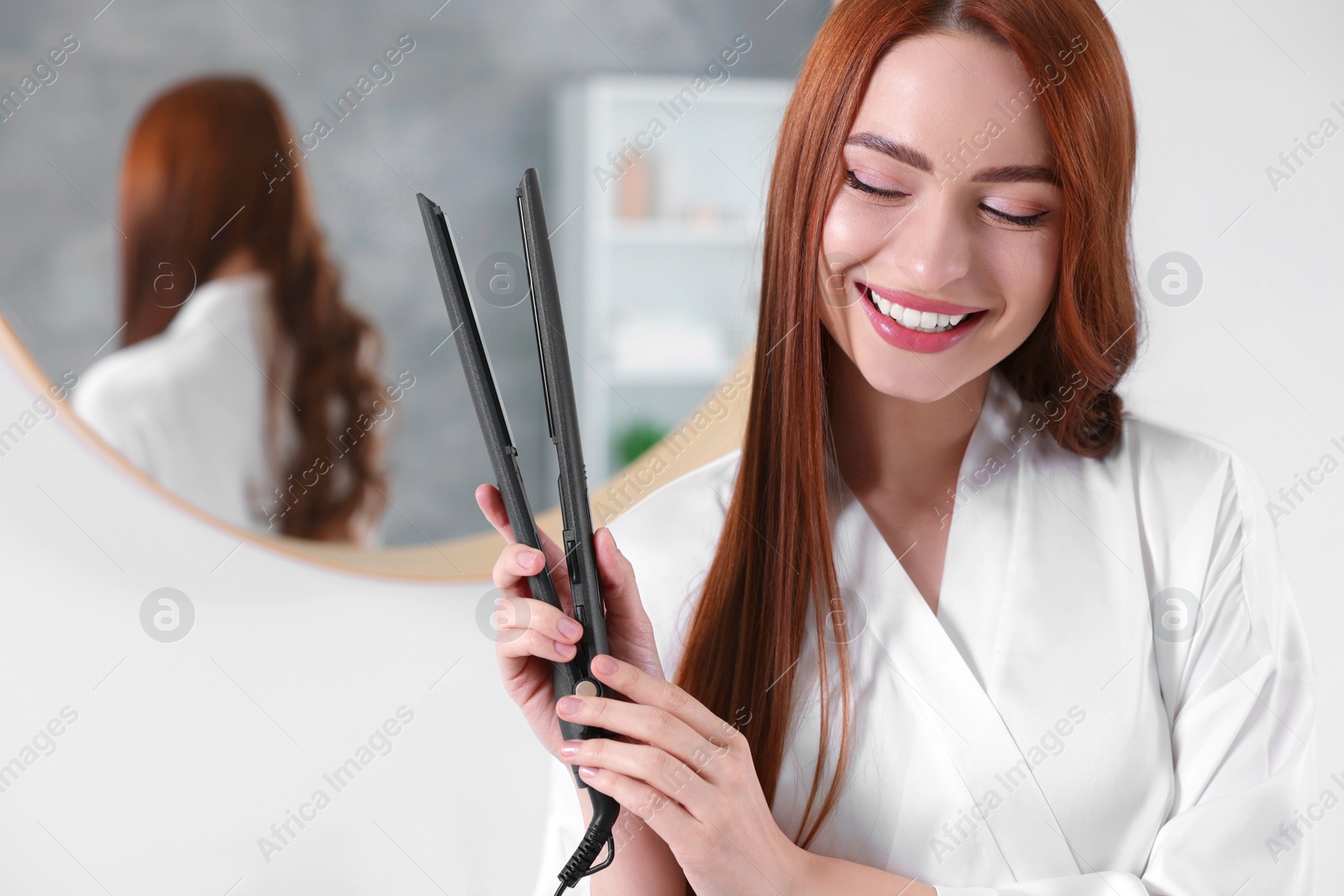 Photo of Beautiful woman with hair iron in room, space for text