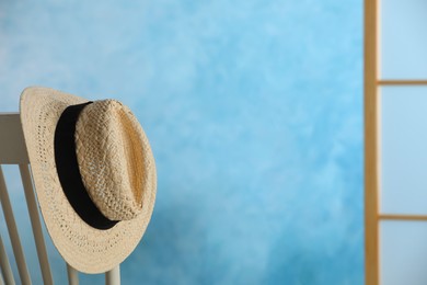 Stylish straw hat hanging on chair in room, space for text