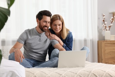 Happy couple with laptop on bed at home