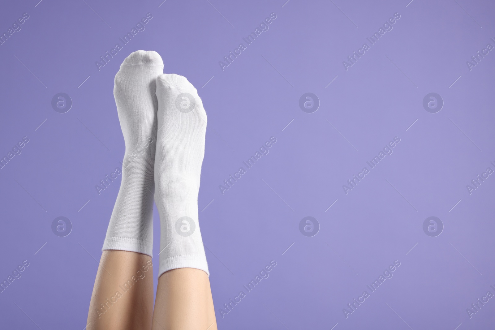 Photo of Woman in stylish white socks on violet background, closeup. Space for text