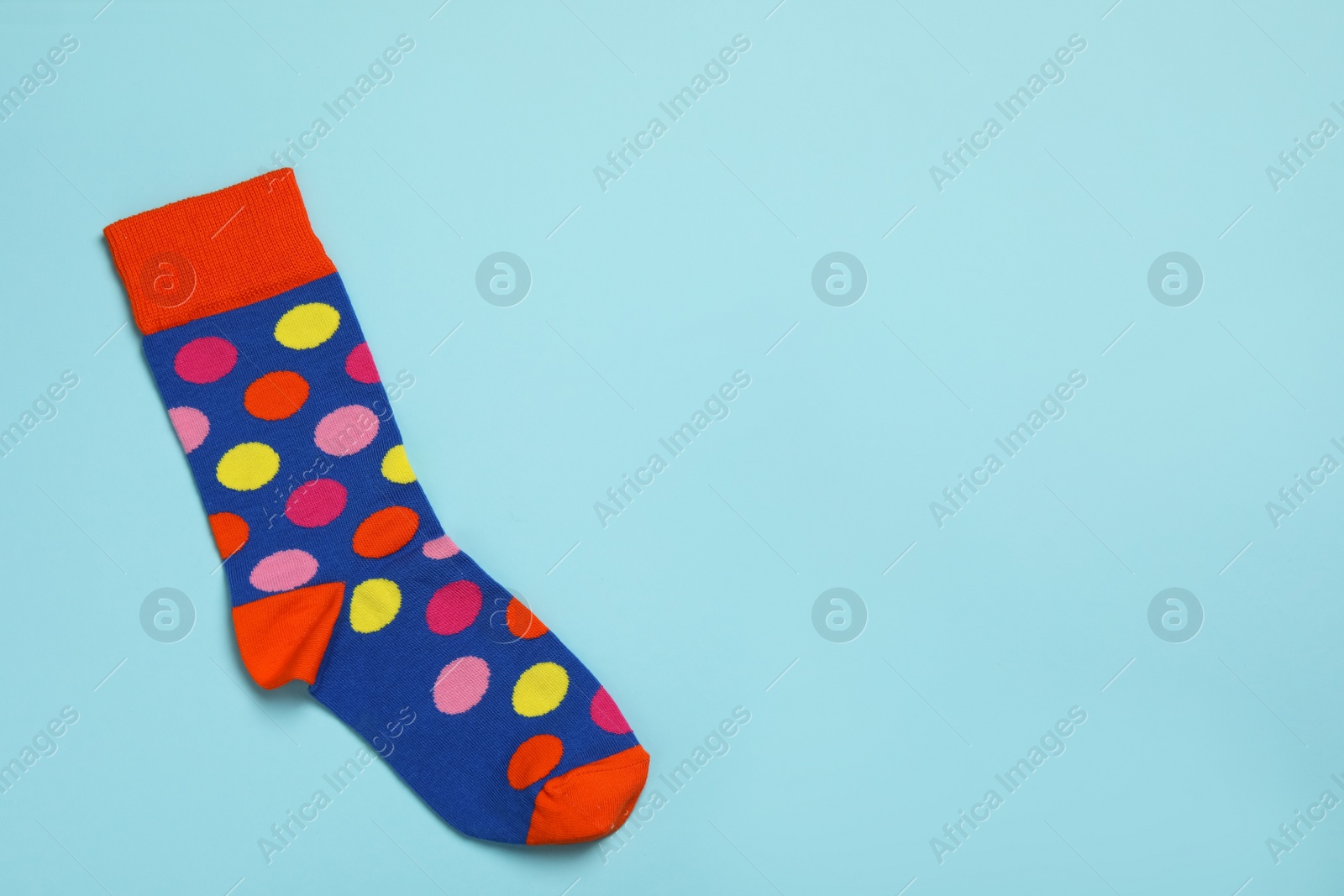 Photo of New sock with pattern on light blue background, top view. Space for text