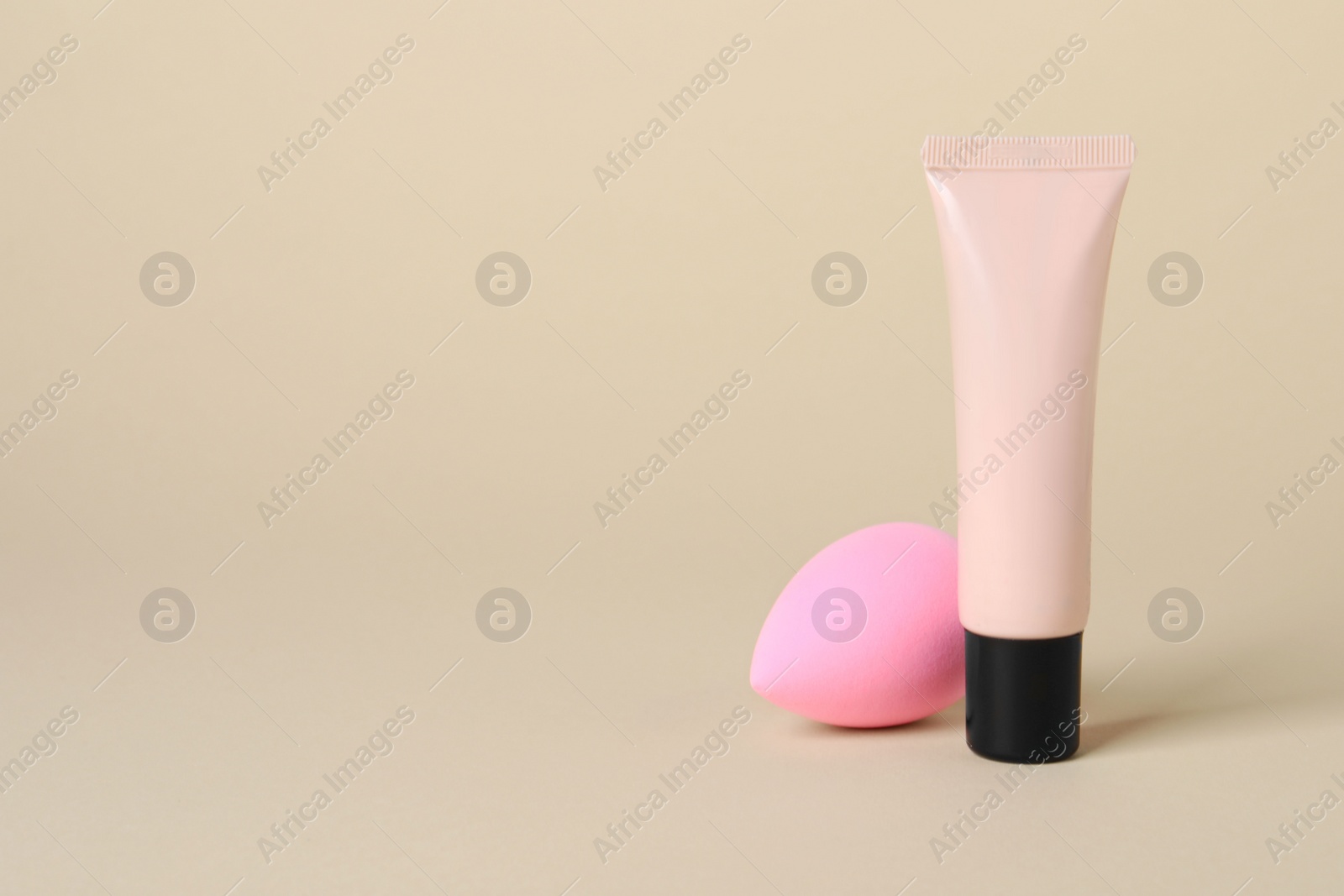 Photo of Tube of skin foundation and sponge on beige background, space for text. Makeup product