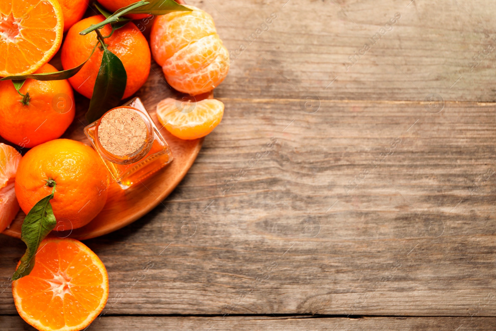 Photo of Bottle of tangerine essential oil and fresh fruits on wooden table, top view. Space for text