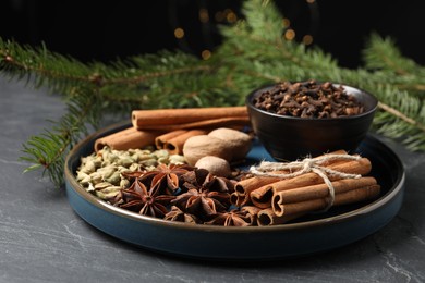 Dishware with different spices, nuts and fir branches on gray table, closeup