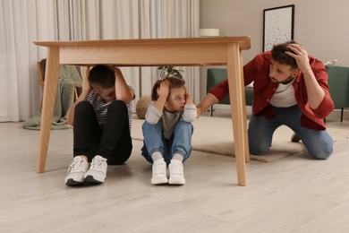 Photo of Father comforting his scared children under table in living room during earthquake